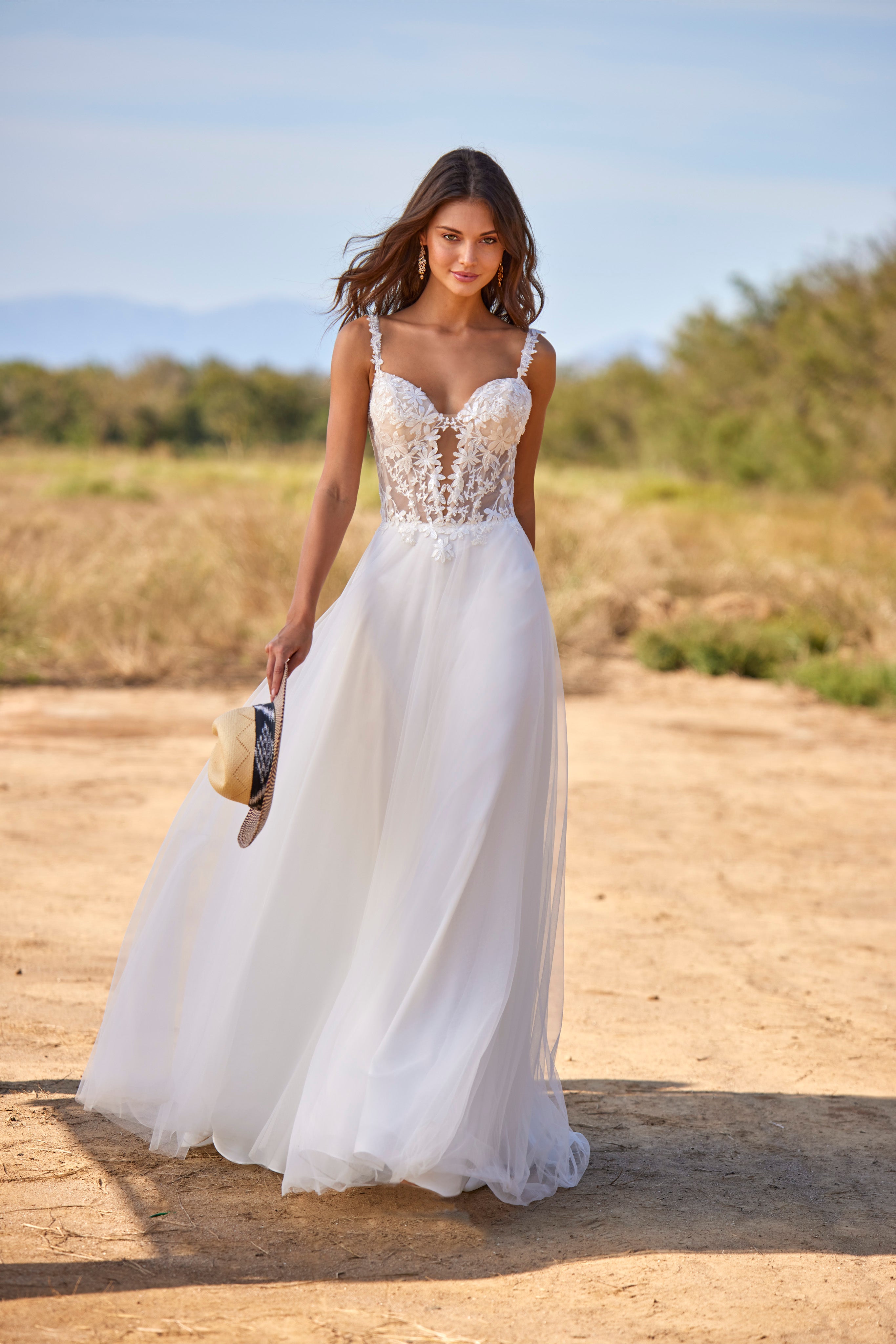 Woman in a white wedding dress standing on a dirt road with trees in the background