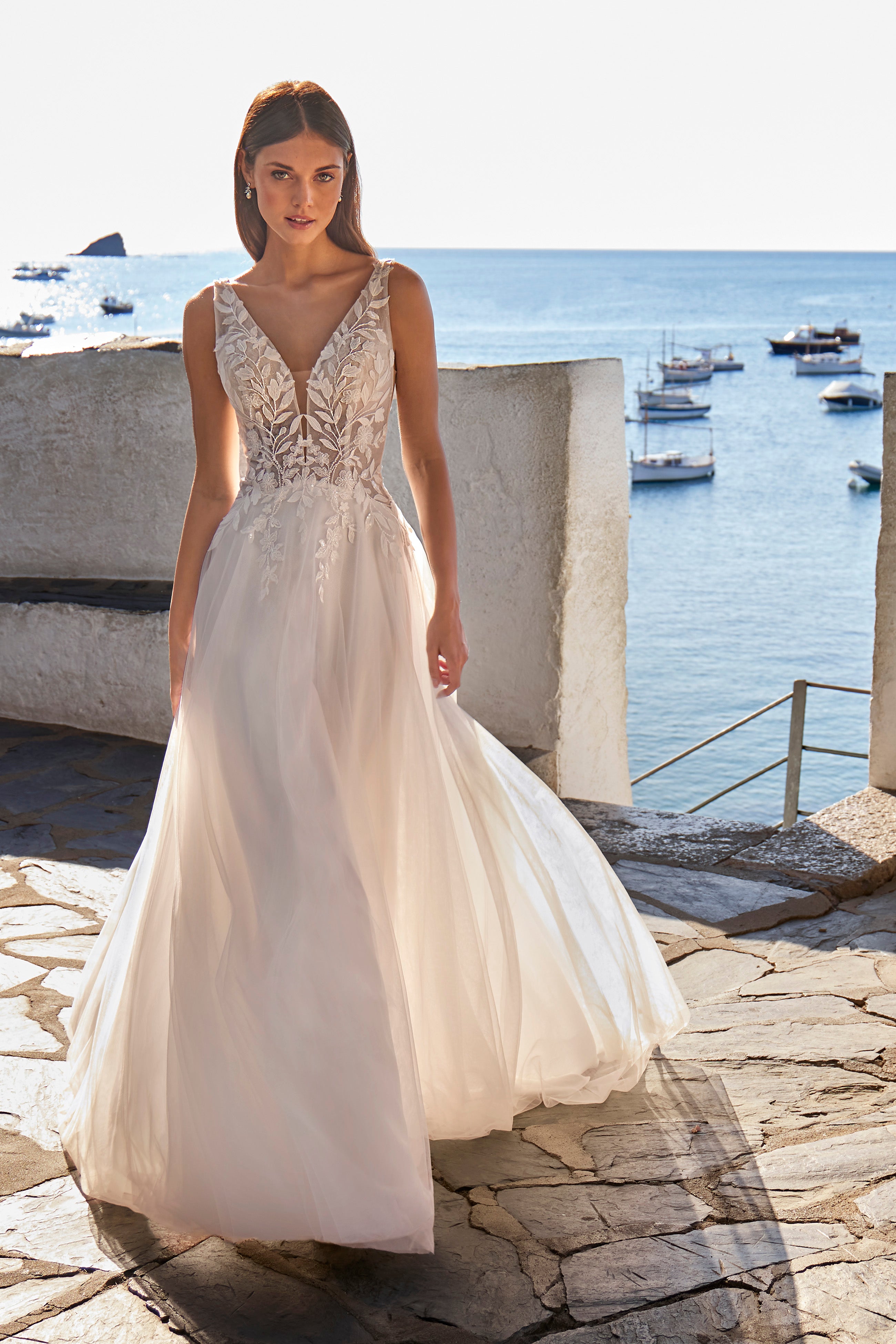 Woman in a white wedding dress standing by the sea with boats in the background