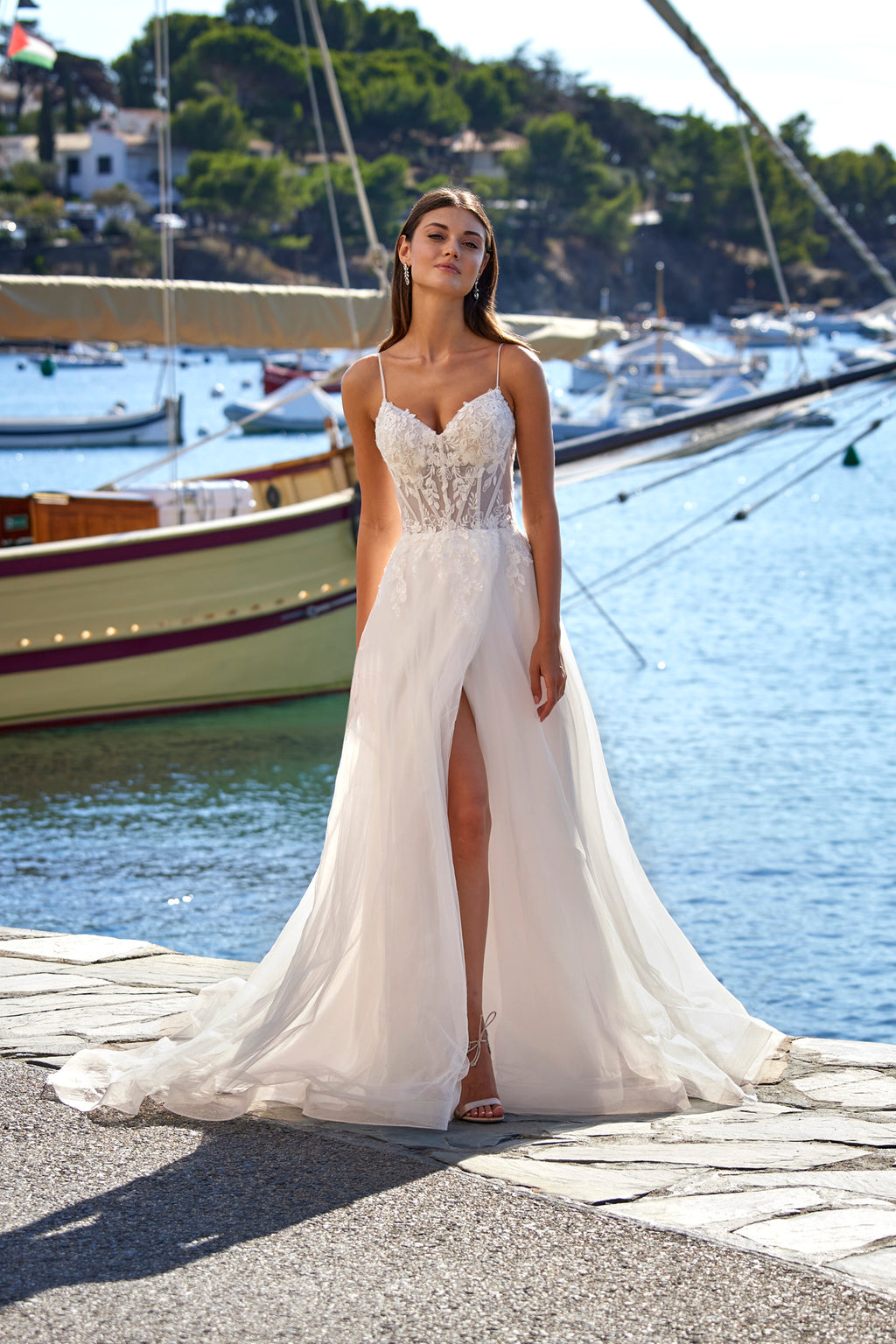 Woman in a white wedding dress standing by a waterfront with boats in the background