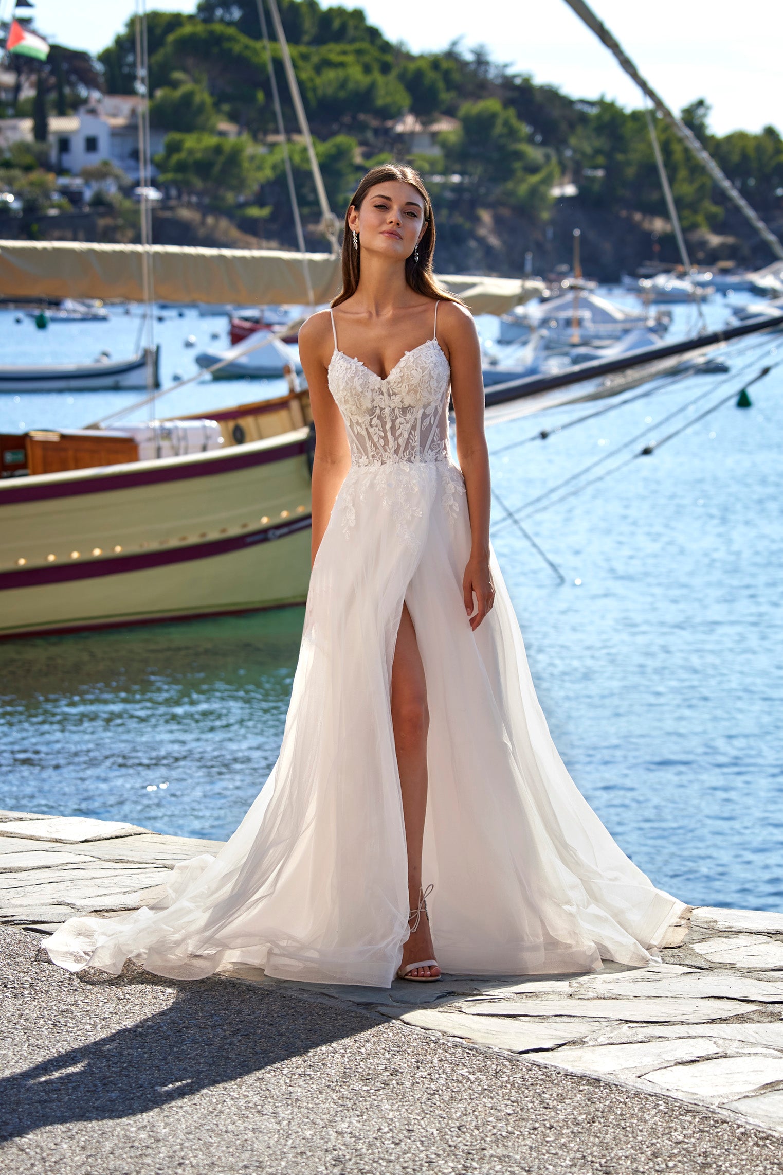 Woman in a white wedding dress standing by a waterfront with boats in the background