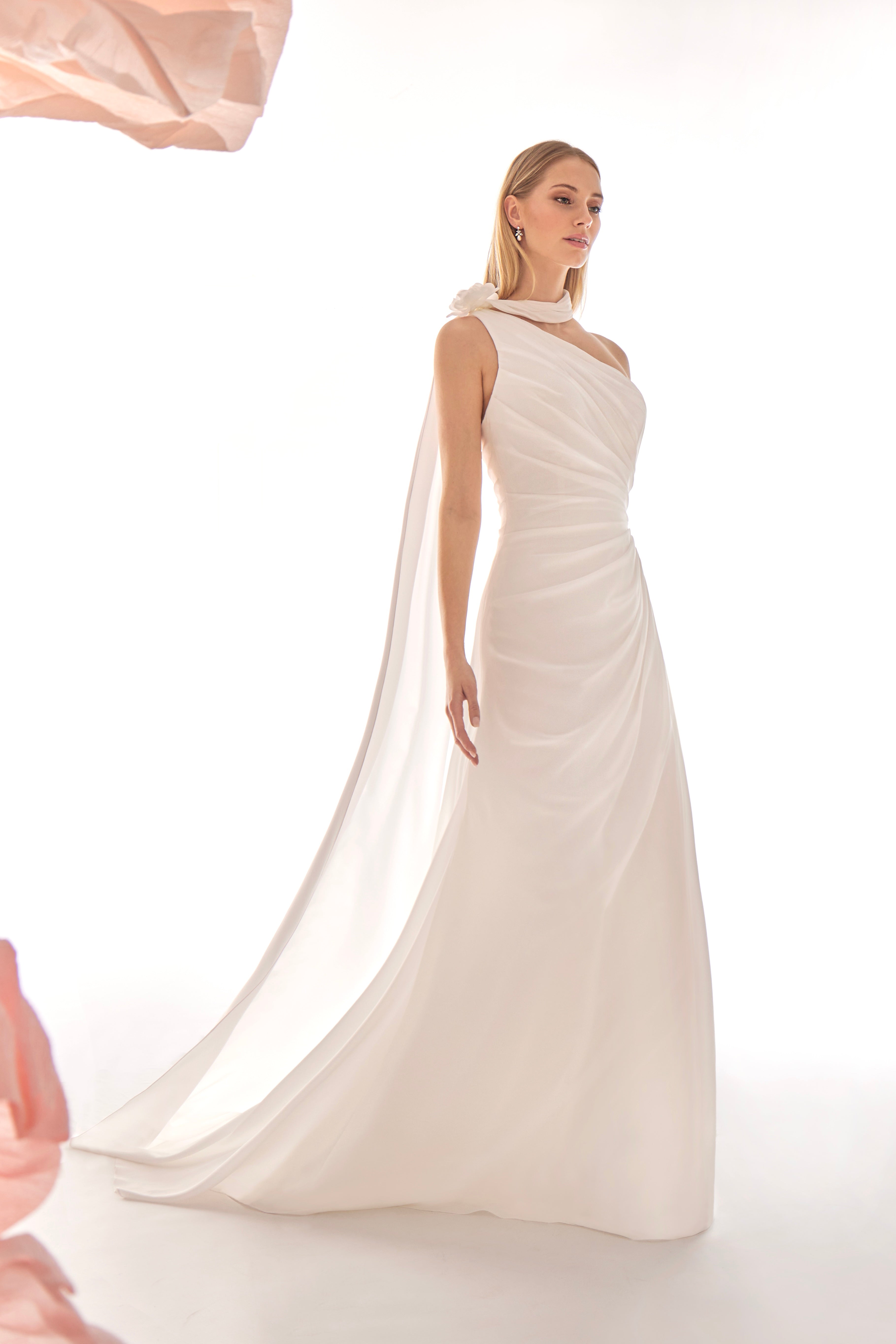 Woman wearing a white one-shoulder gown with a flowing train on a white background