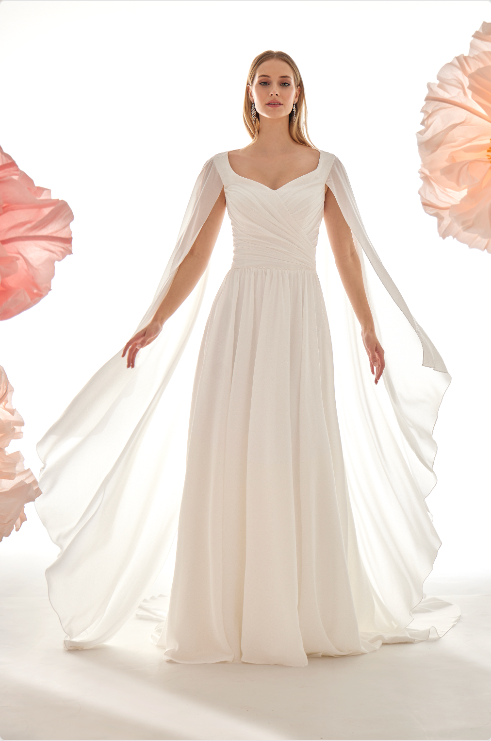Woman wearing a white wedding dress with a cape against a white background